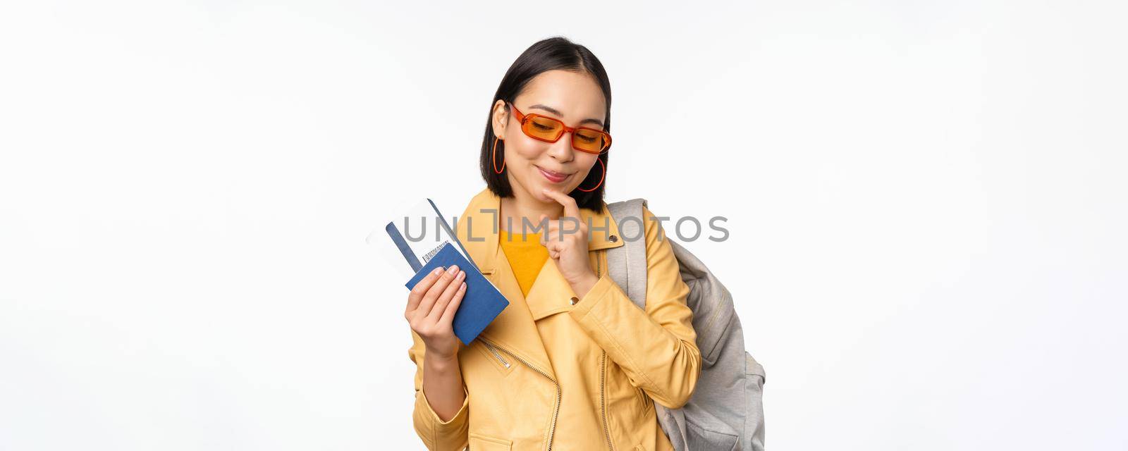 Asian girl tourist with boarding tickets and passport going abroad, holding backpack, thinking of travelling, standing over white background by Benzoix