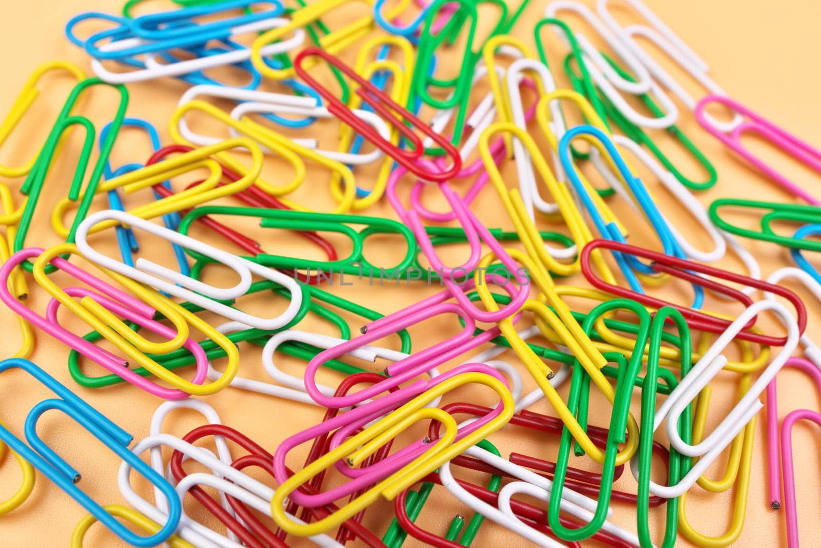 Full Frame High Angle View of Multicolored Paperclips Isolated on a Cheerful Orange Beige Background with shallow depth of field. High quality photo