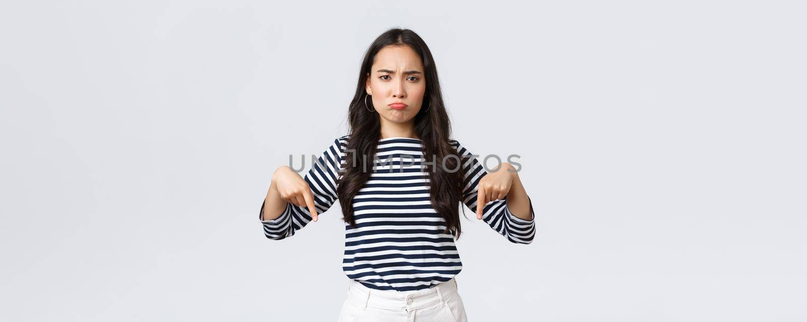 Lifestyle, beauty and fashion, people emotions concept. Disappointed upset young asian woman pouting and frowning displeased, pointing fingers down as complaining about product or service.