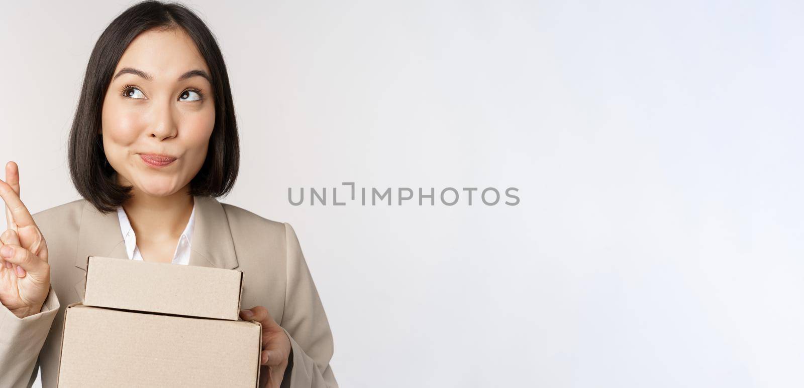 Hopeful asian entrepreneur, business woman holding boxes with customer order, making wish, wishing and anticipating, standing over white background.