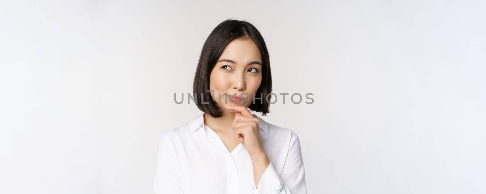 Close up portrait of asian woman thinking, looking aside and pondering, making decision, standing over white background by Benzoix