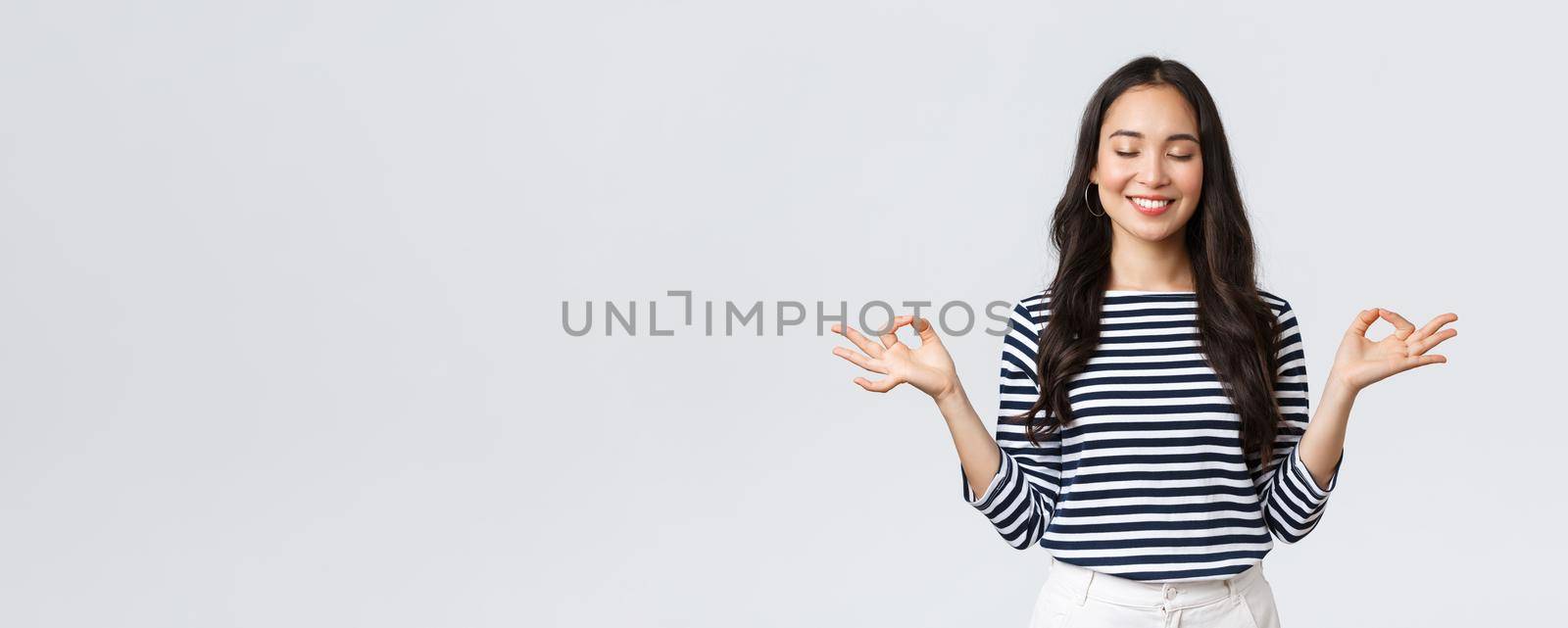 Lifestyle, people emotions and casual concept. Calm happy young woman feeling peaceful during meditation, close eyes and smiling as hold hands in zen nirvana gesture, do yoga exercise by Benzoix