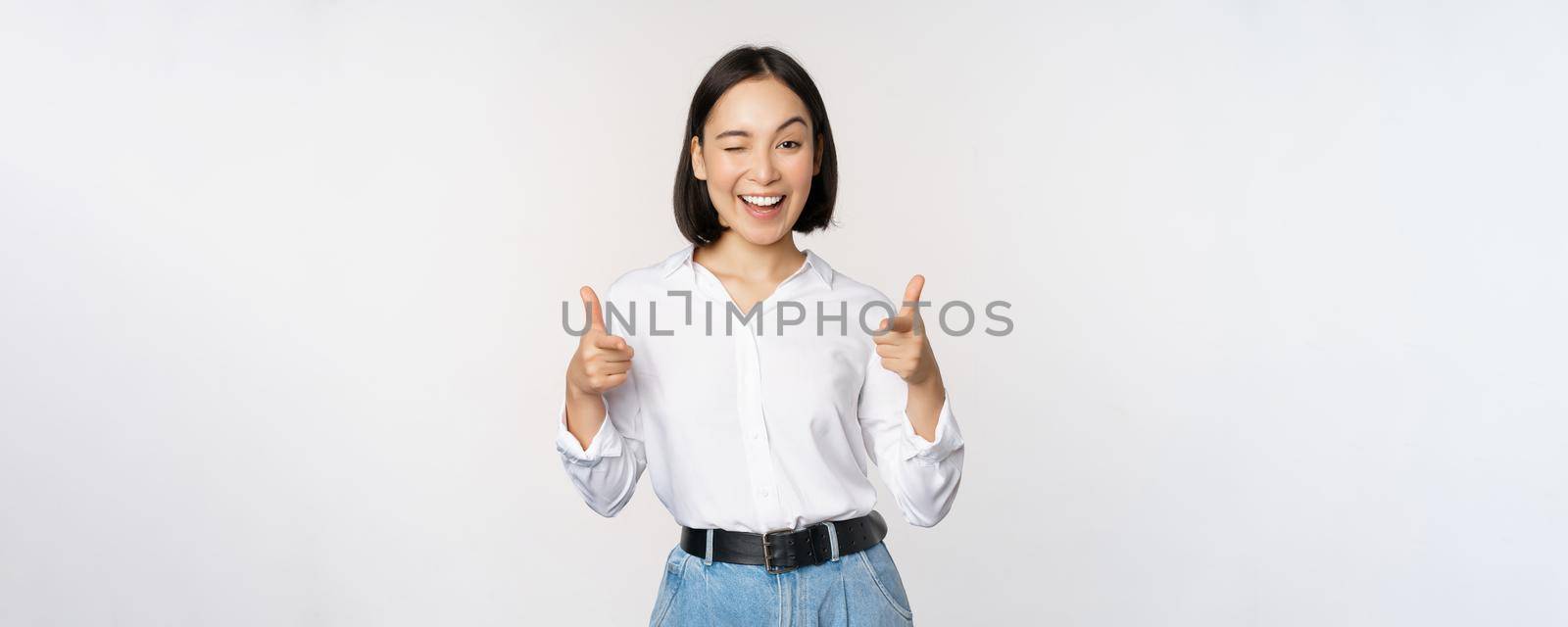 Its you congrats. Smiling attractive asian woman, businesswoman pointing fingers at camera with pleased face, complimenting, inviting you, standing over white background.