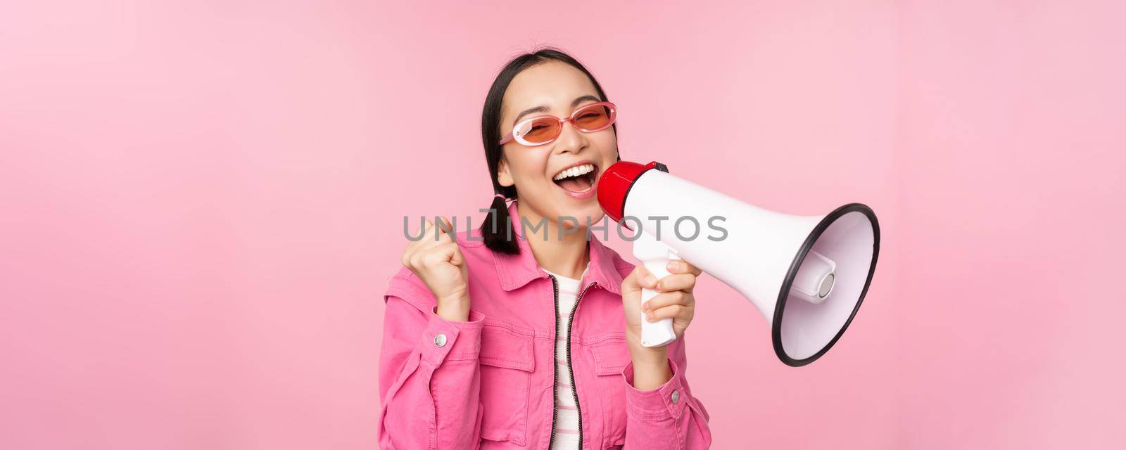 Attention, announcement concept. Enthusiastic asian girl shouting in megaphone, advertising with speaker, recruiting, standing over pink background by Benzoix