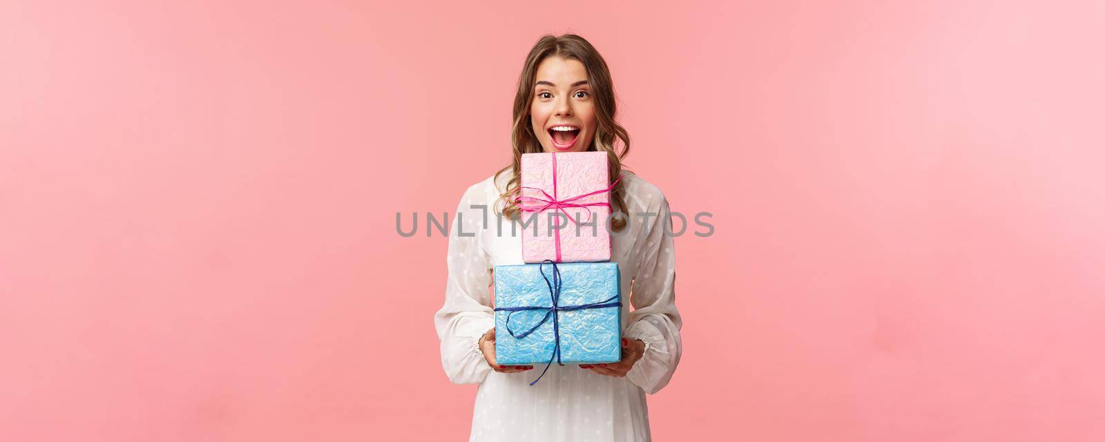 Holidays, celebration and women concept. Portrait of happy cheerful girl likes celebrating birthday and receive presents, holding two gift boxes and smiling camera, pink background by Benzoix
