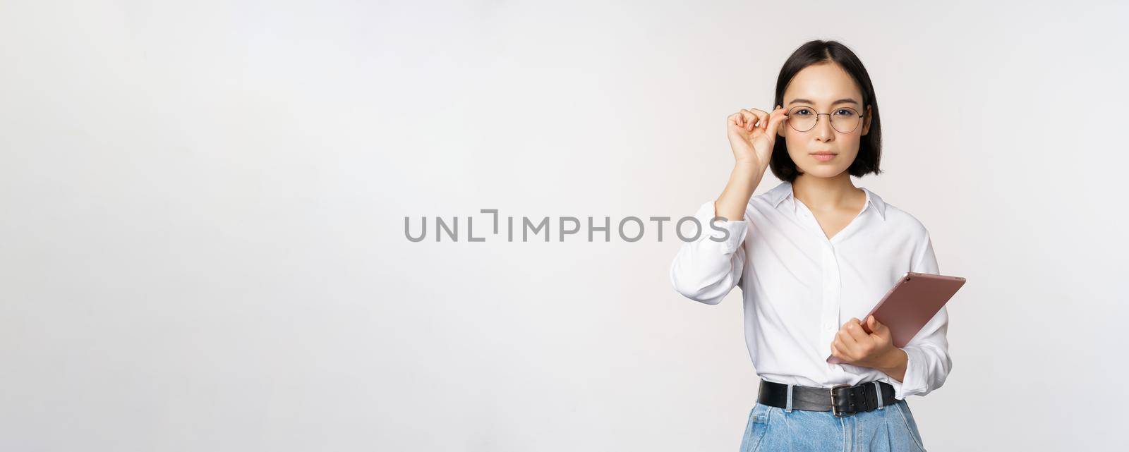 Image of young asian business woman, female entrepreneur in glasses, holding tablet and looking professional in glasses, white background.