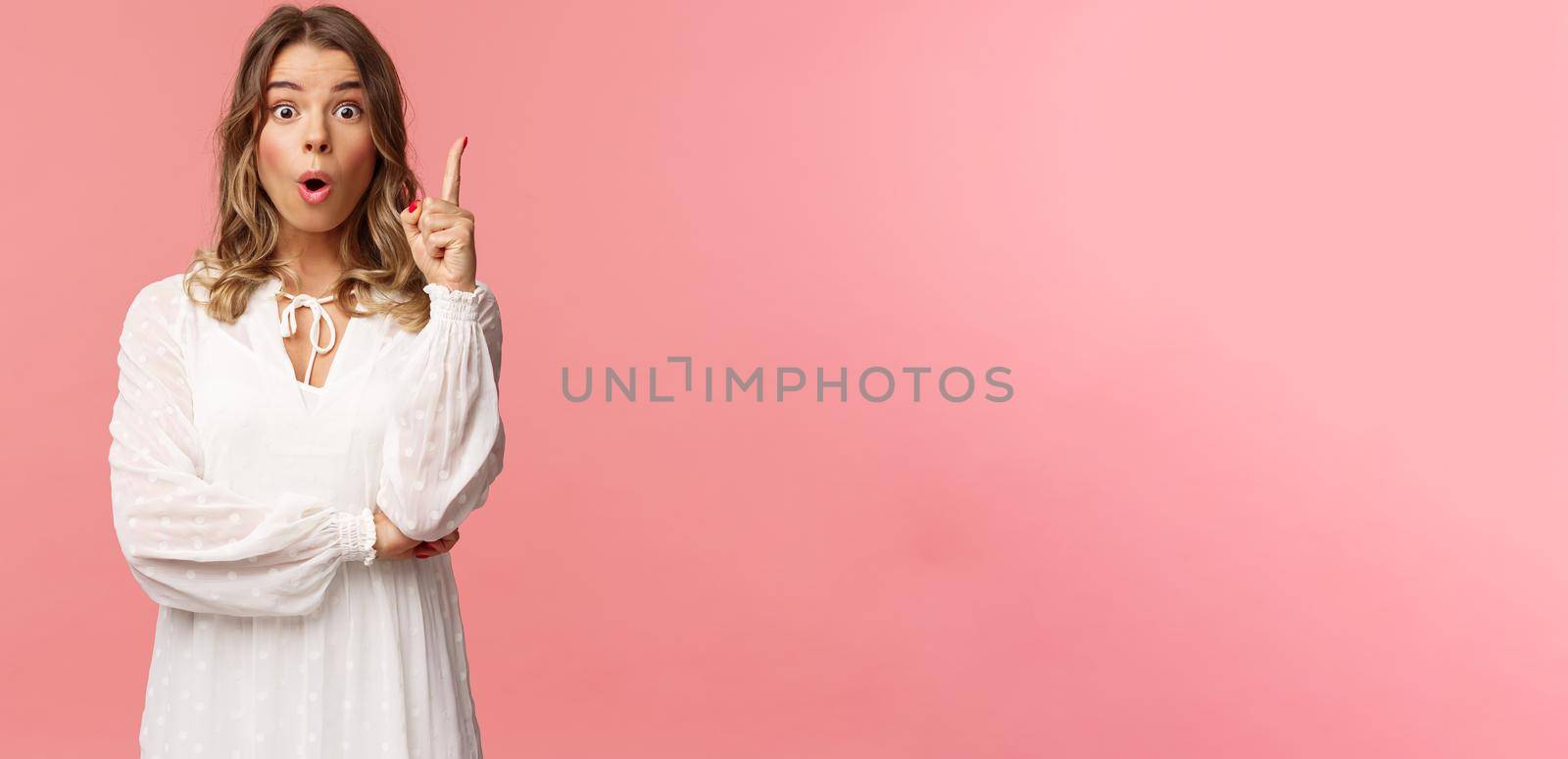 Beauty, fashion and women concept. Portrait of amazed and excited feminine blond girl in white dress, open mouth gasping amused and raise one finger, have suggestion, found solution.