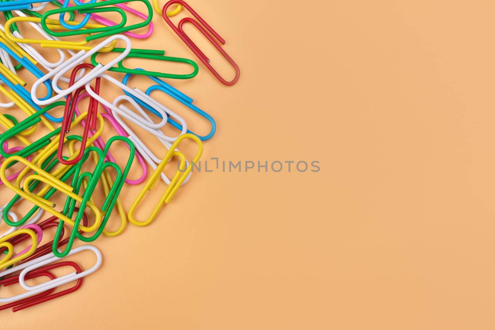 Multicolored Paperclips Isolated on a Cheerful Orange Beige Background with Copy Space on Right. High quality photo