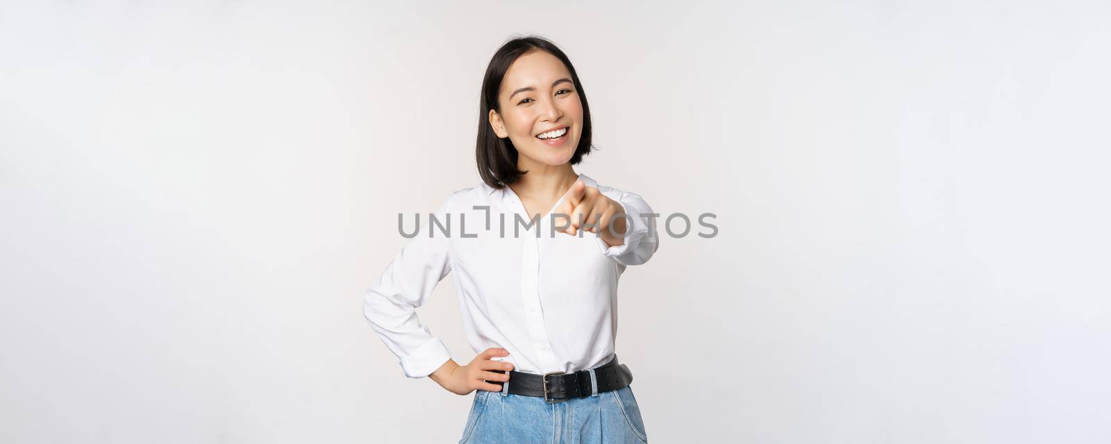 Its you. Beautiful young asian woman, company manager pointing finger at camera and smiling, choosing, inviting people, recruiting, standing over white background.