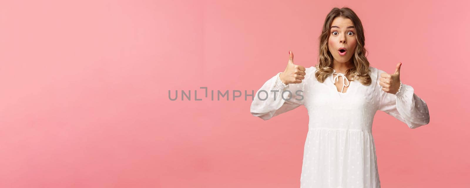 Portrait of amazed, excited blond young girl in white cute dress, open mouth say wow astonished and fascinated, show thumbs-up like and approve, beaing satisfied, pink background by Benzoix