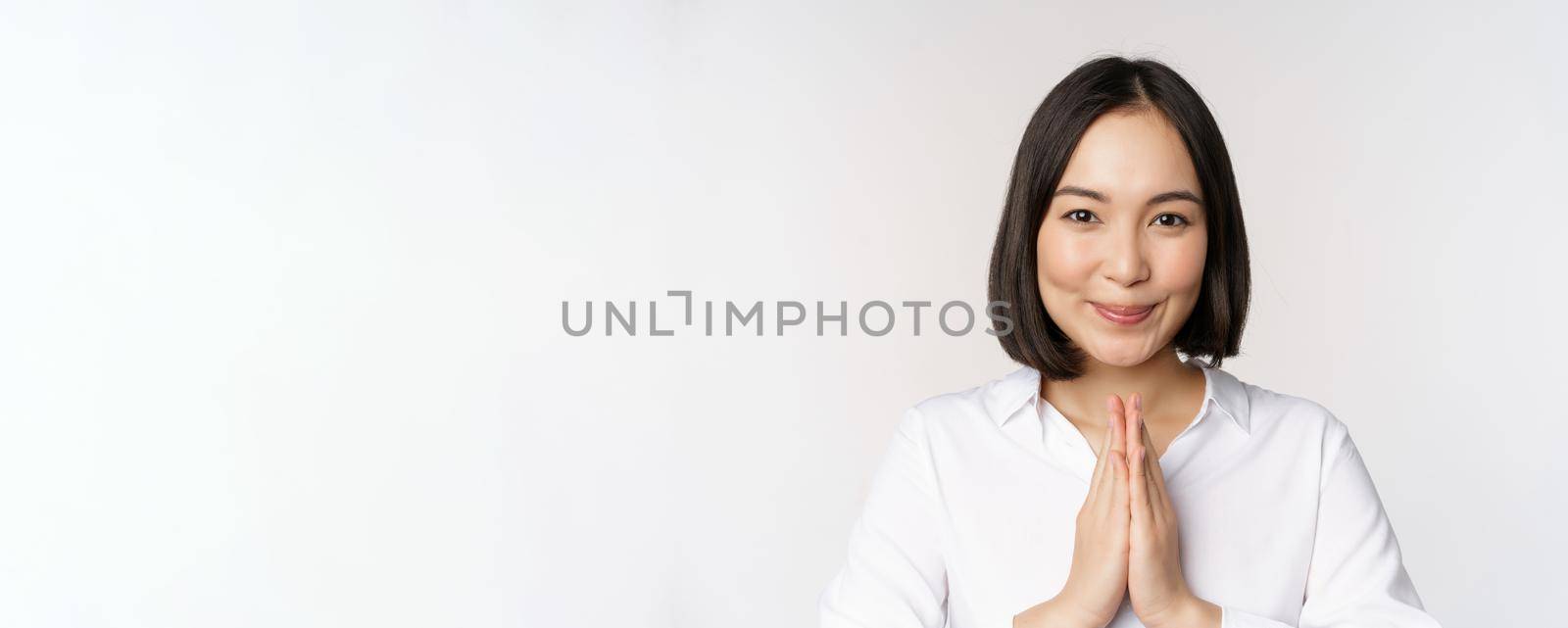 Close up portrait of young japanese woman showing namaste, thank you arigatou gesture, standing over white background.