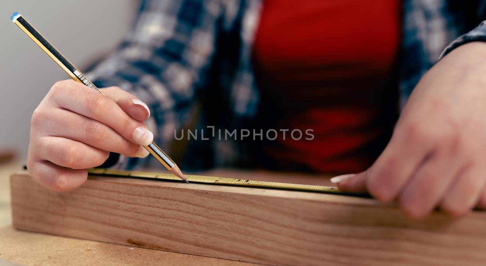 Detail of the hands of a young woman measuring a strip of wood for the manufacture of a piece of furniture. by CatPhotography