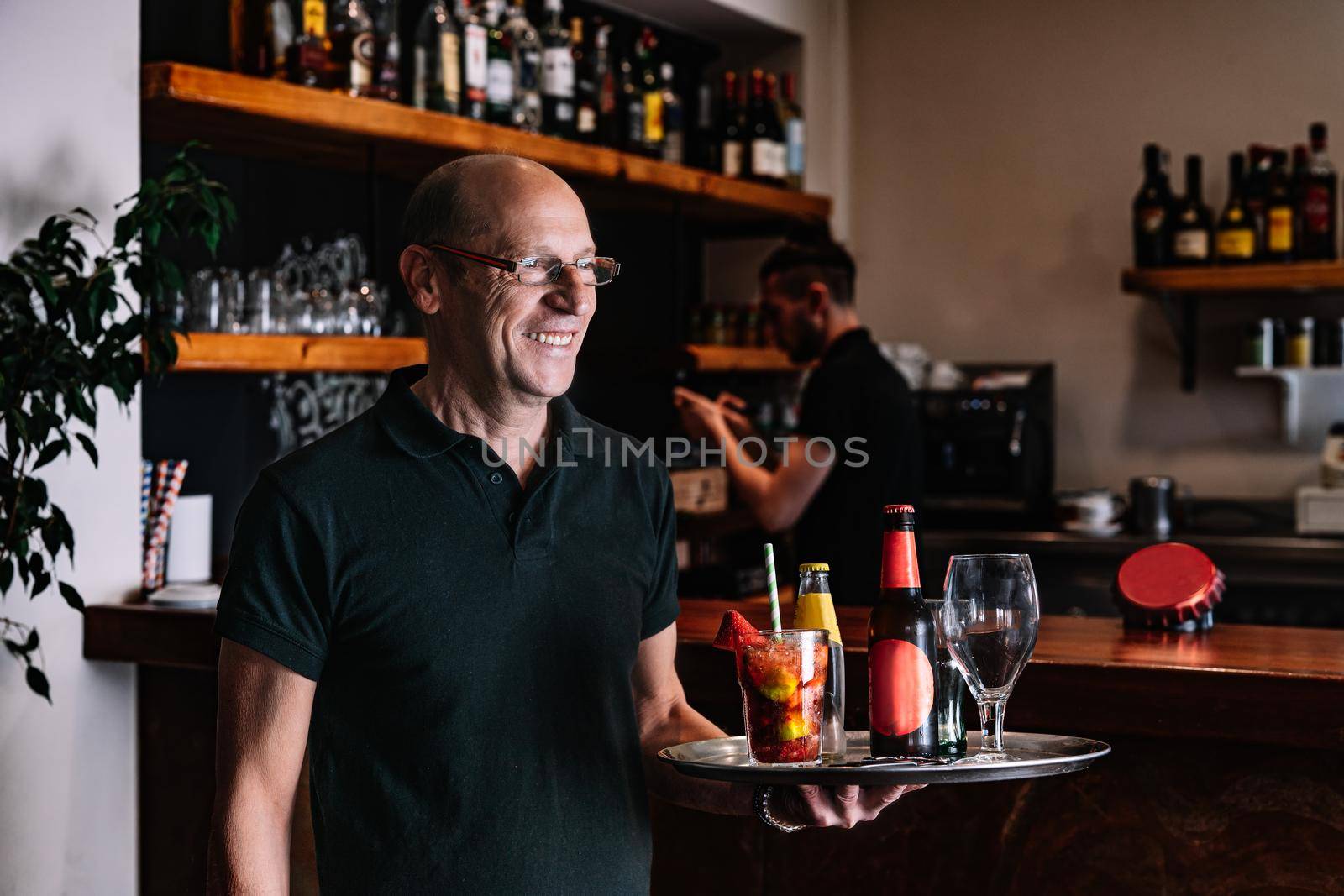 Mature, smiling waiter holding a tray with his hands. Worker in his small business carrying a tray of drinks. by CatPhotography