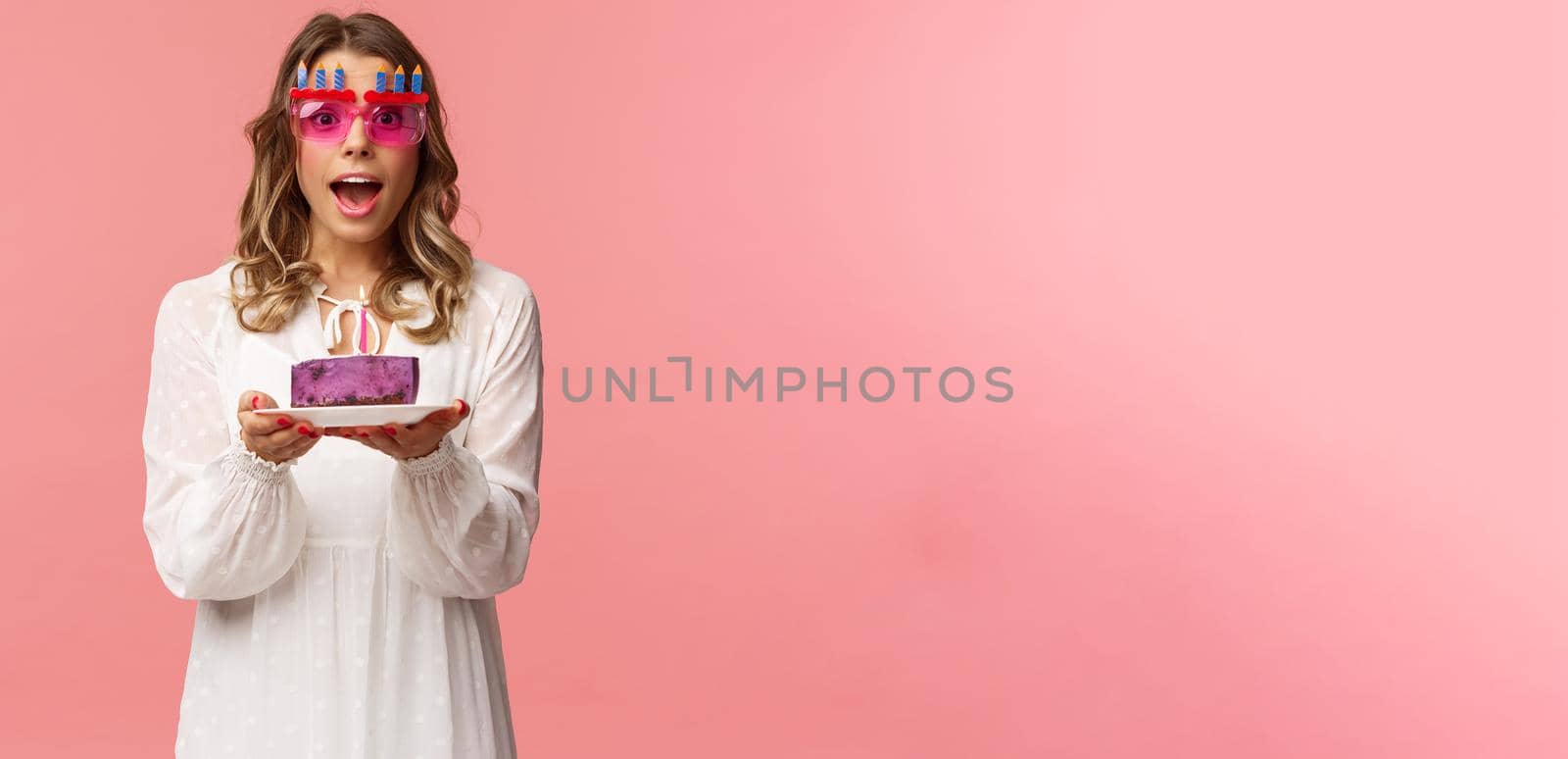 Holidays, spring and party concept. Excited, happy attractive blond woman in white dress, wearing funny b-day glasses, holding birthday cake with lit candle, making wish smiling camera by Benzoix