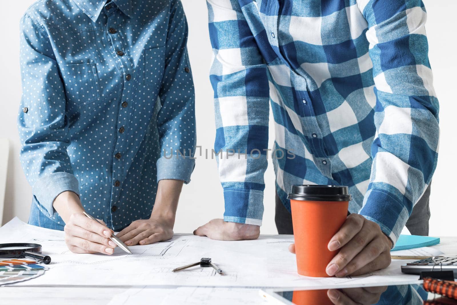 Man and woman together working at design project. Creative teamwork at workspace with construction blueprint and color swatches. People standing near desk and discussing in architecture studio.