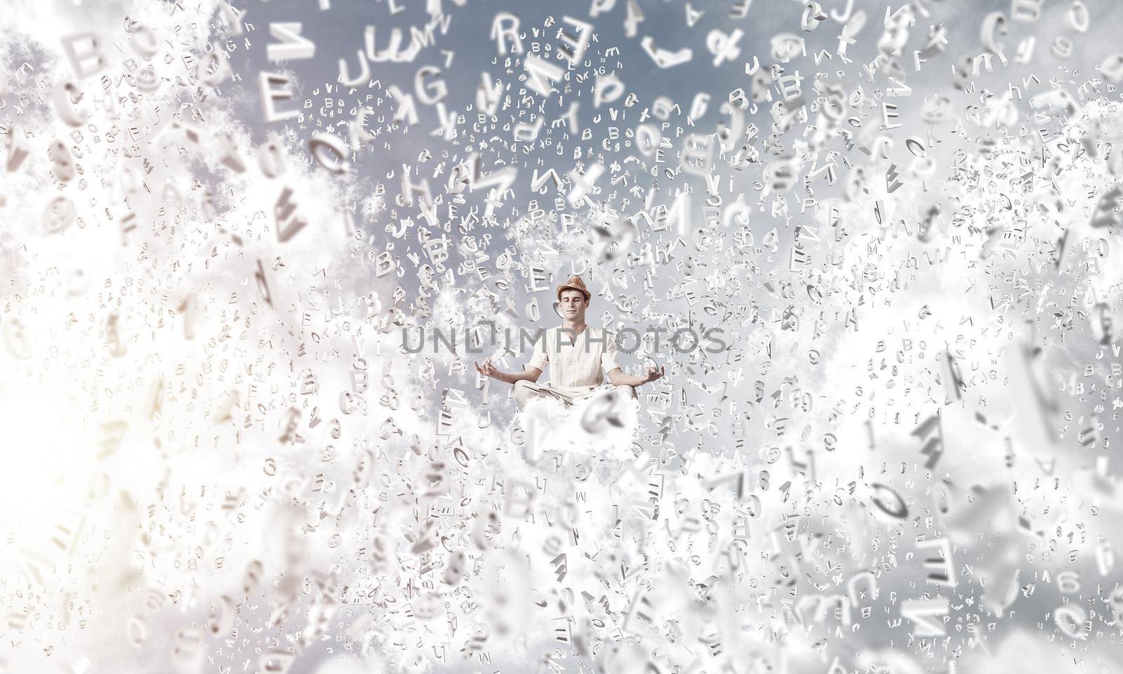 Man in white clothing keeping eyes closed and looking concentrated while meditating among flying letters in the air with cloudy skyscape on background.