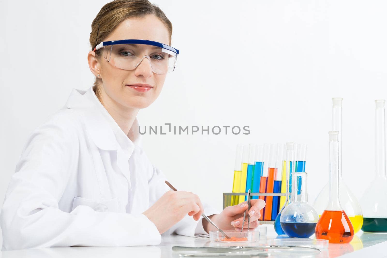 Microbiologist researching biomaterial with tweezers in petri dish. Molecular biology laboratory analysis and genetic experimentation. Beautiful woman scientist in protective goggles at workplace.
