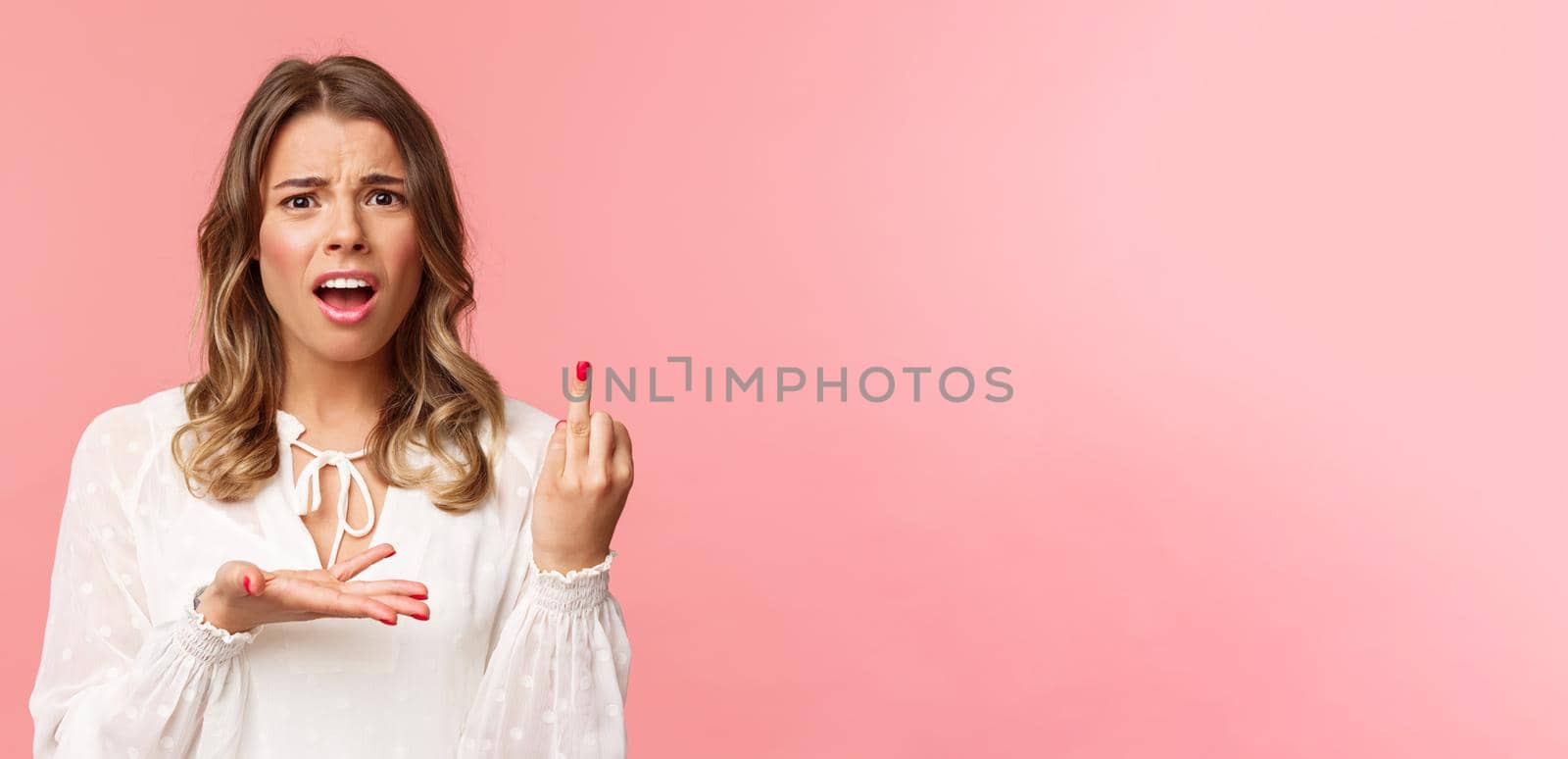 Close-up portrait of frustrated pissed-off, complaining beautiful girl tired of waiting for proposal, pointing at ring finger with bothered grimace, standing pink background disappointed by Benzoix