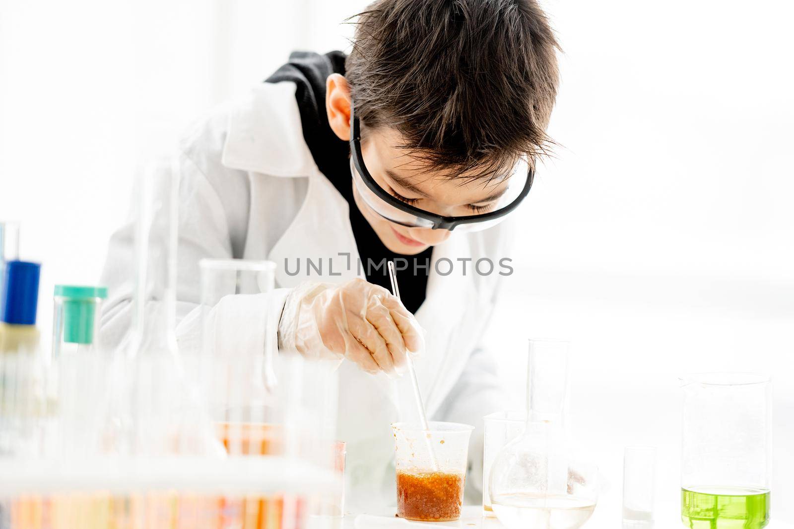 School boy wearing protection glasses doing chemistry experiment in elementary science class and mix components. Clever pupil in lab during test
