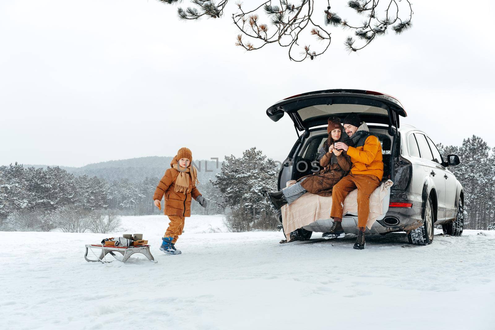 Winter portrait of a family sit on car trunk enjoy their vacation in forest by Fabrikasimf