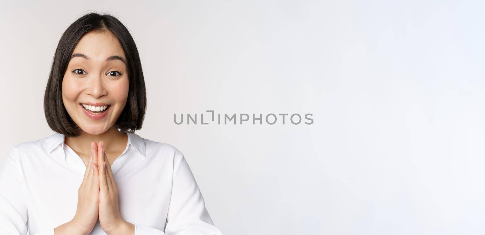 Close up portrait of young japanese woman showing namaste, thank you arigatou gesture, standing over white background.