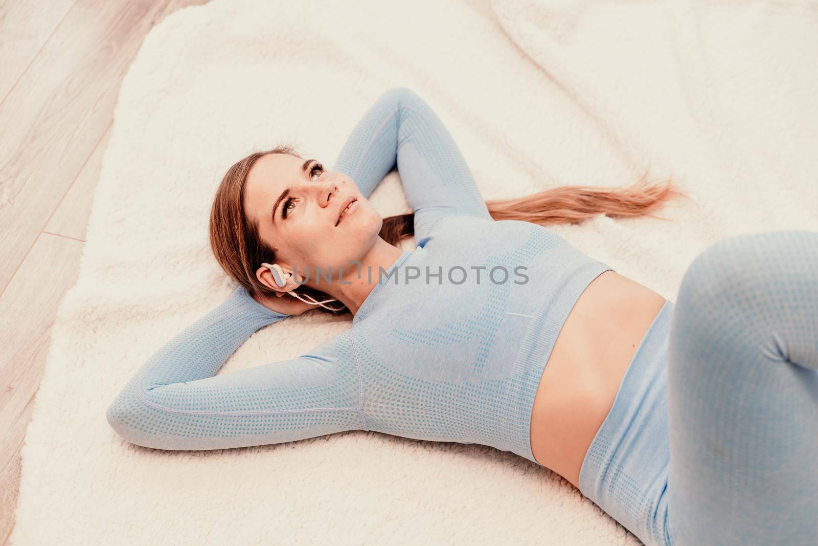 Top view portrait of relaxed woman listening to music with headphones lying on carpet at home. She is dressed in a blue tracksuit