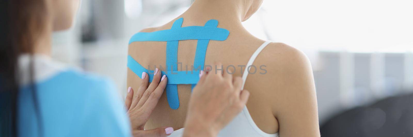 Close-up of doctor applying blue tape on patients back, problem with back, kinesiology helps fight with pain, faster recovery. Physiotherapy, rehabilitation, healthcare concept