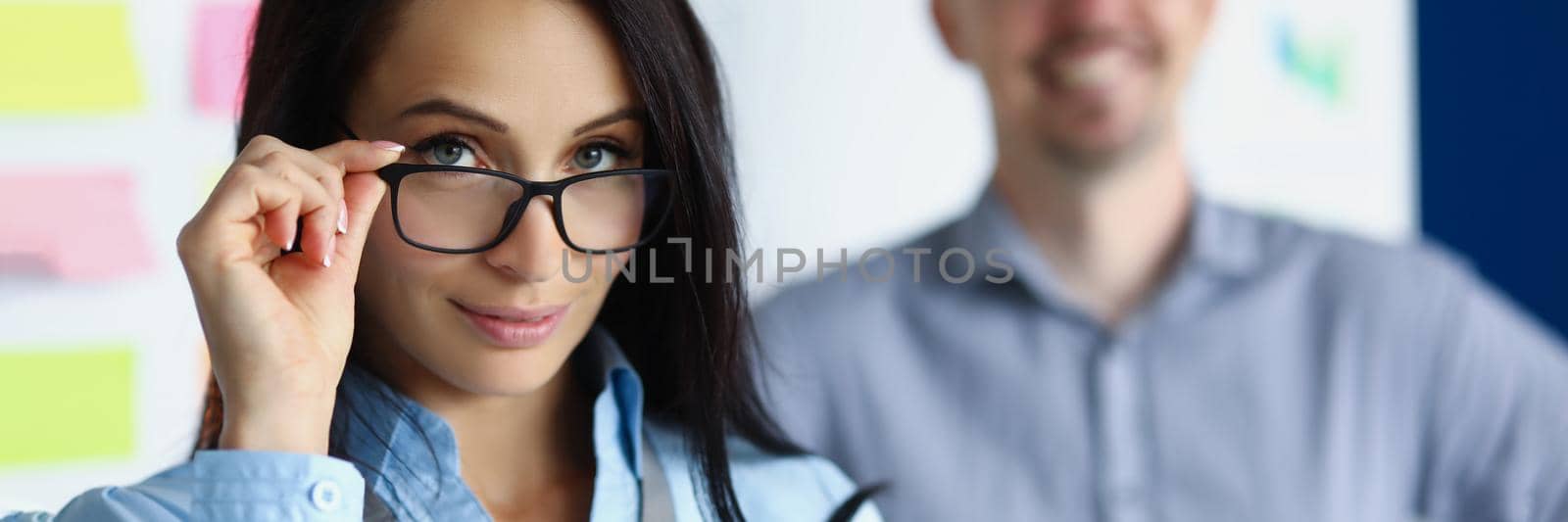 Portrait of pretty woman employee doing her glasses. Work as team on new project. Smiling male colleague on background. Company worker, business presentation, teamwork concept