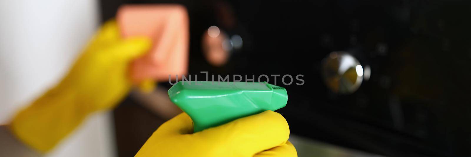 Close-up of woman housekeeper wiping dust from oven using spray and fabric, keep surface clean and shiny at home. Cleaning service job, cleanup, sanitizing, clean space concept. Blurred background