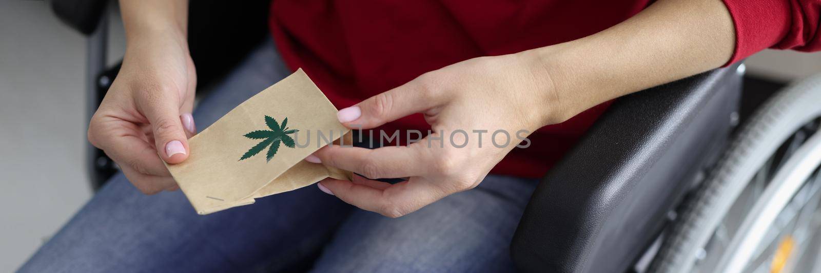 Close-up of woman hands holding package with hemp plant, person sit in wheelchair medication for treatment. Hope for faster healing. Alternative medicine, healthcare, disabled people concept