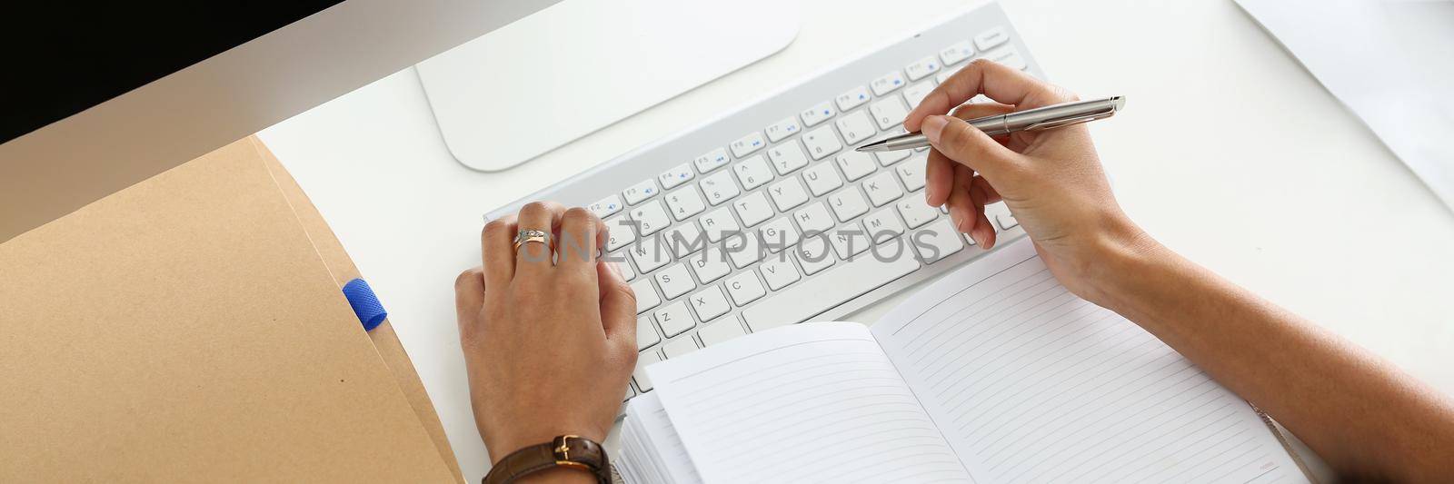 Top view of modern working place with laptop, keyboard, notebook. Woman typing and making notes in open diary. Copy space, mockup, workplace, office, technology, secretary concept