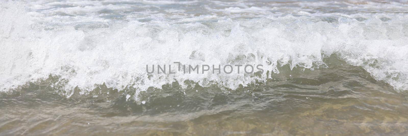 Close-up of blue sea waves, sandy coastline, choppy sea, clean water. People on horizon swimming in water. Beach, ocean, black sea, holiday, summer, relaxation concept