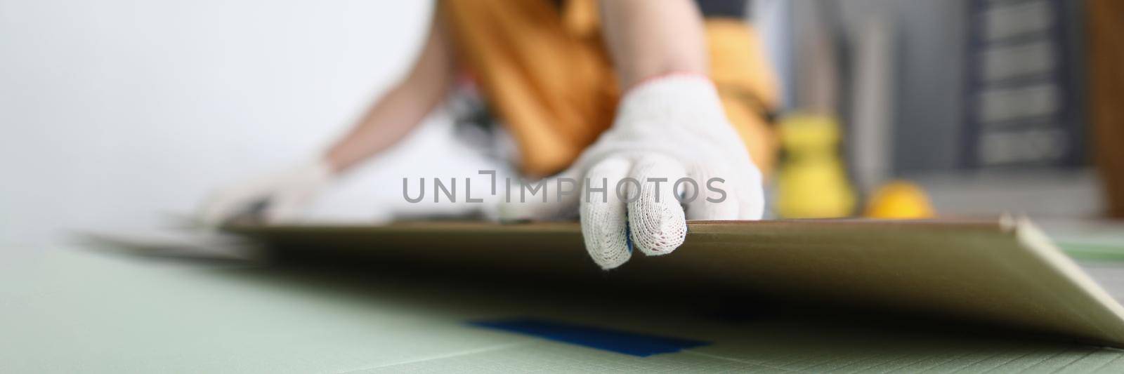 Close-up of carpenter laying wooden panel of laminate floor, installing new floor for apartment. Qualified worker deal with parquet pieces. Home renovation, construction concept. Blurred background