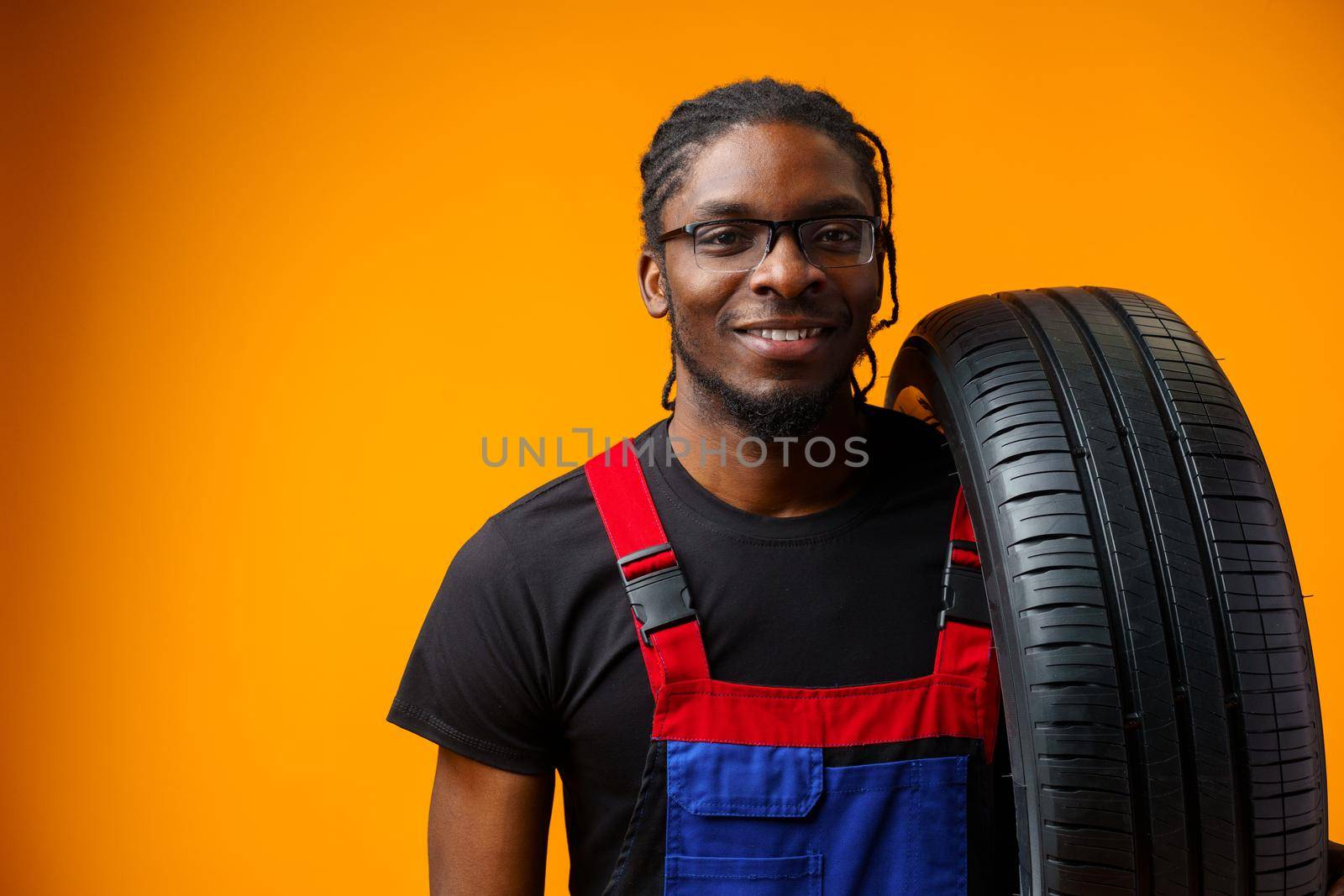 African american car service worker with car tyre against yellow background, close up
