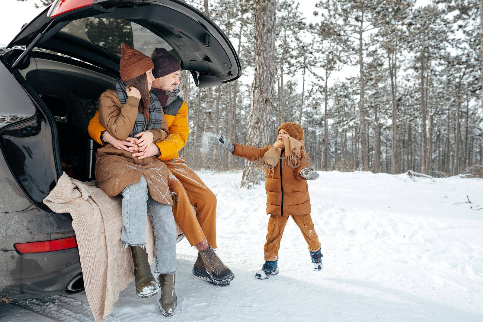 Lovely smiling couple sitting in car trunk in winter forest by Fabrikasimf