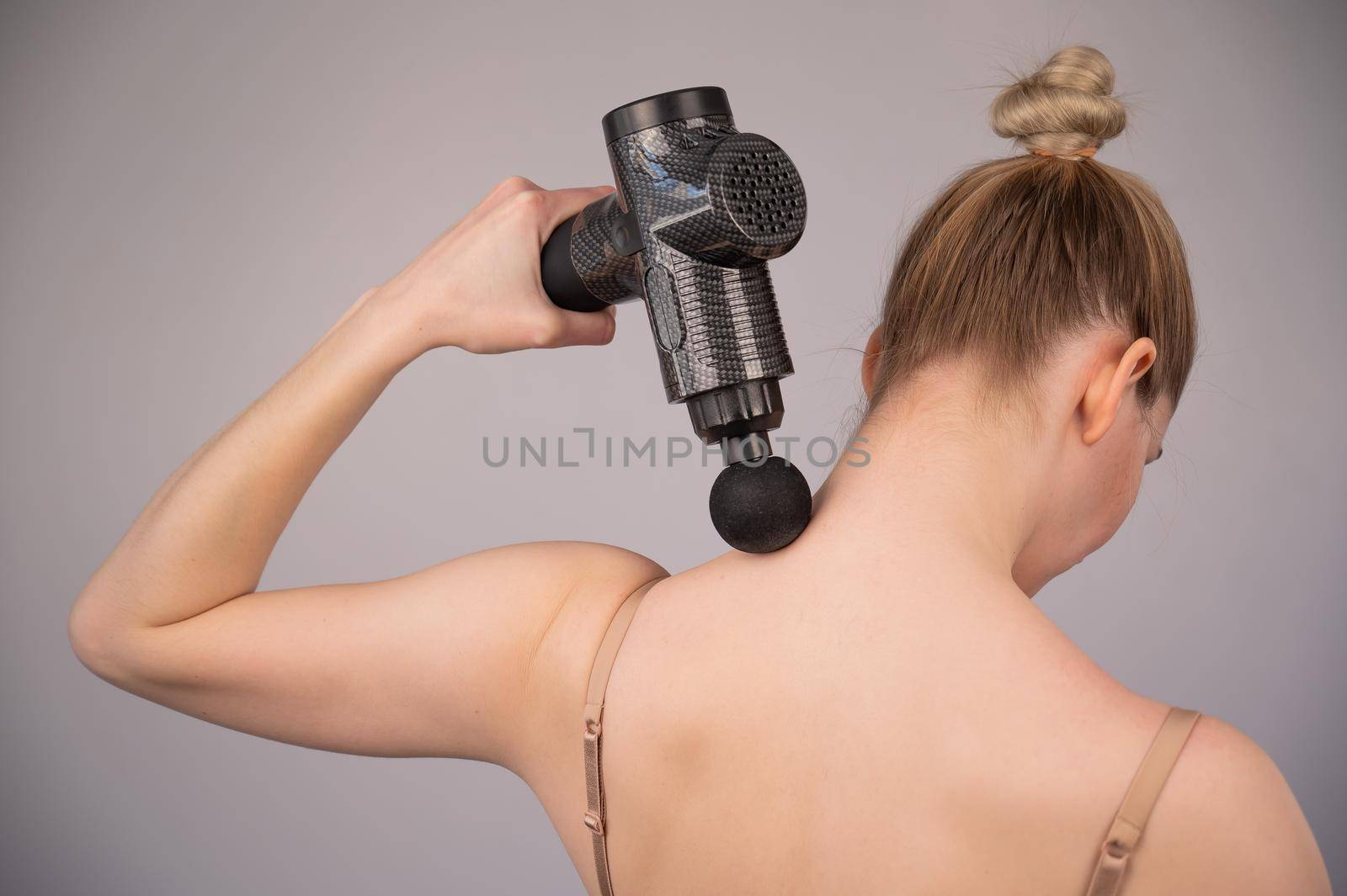 Caucasian woman giving herself a back massage with a gun