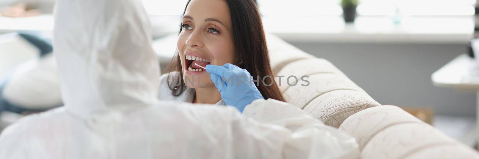 Portrait of doctor or laboratory assistant in protective suit takes swab from throat of sick patient, perform procedure at home, lab test for coronavirus. Quarantine, pandemic, health concept