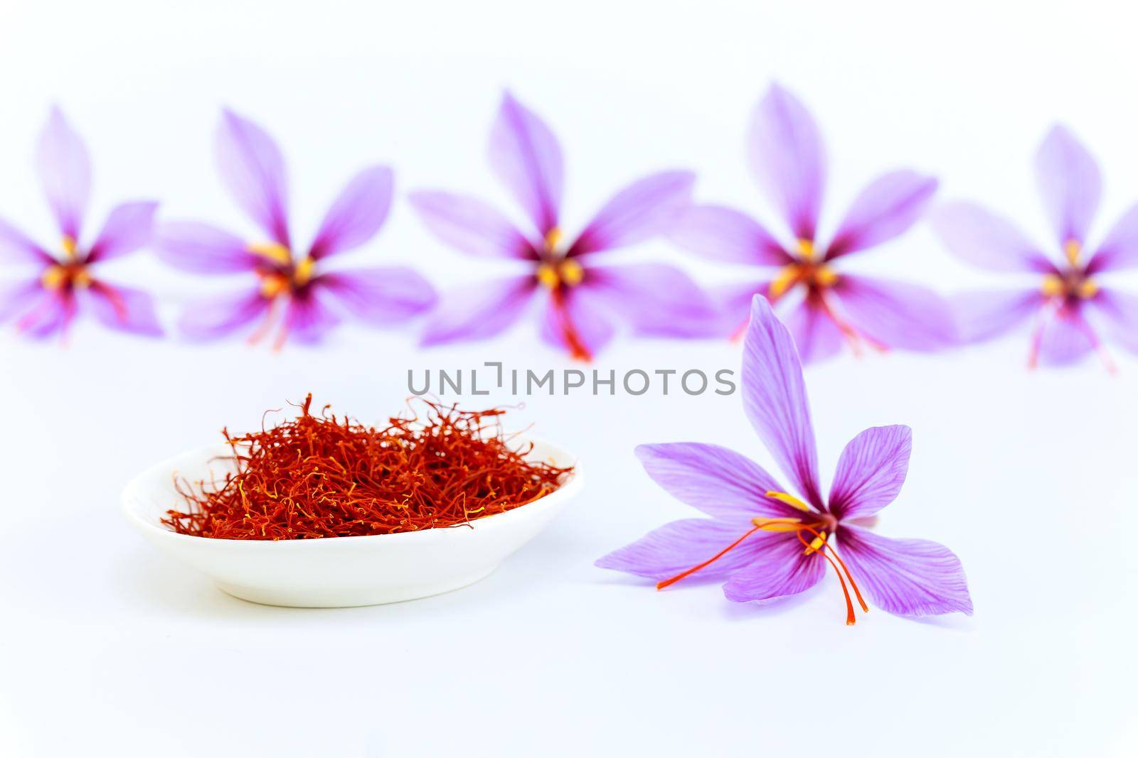 Dry saffron stamens in a white plate and crocuses on a white background. Saffron spice.