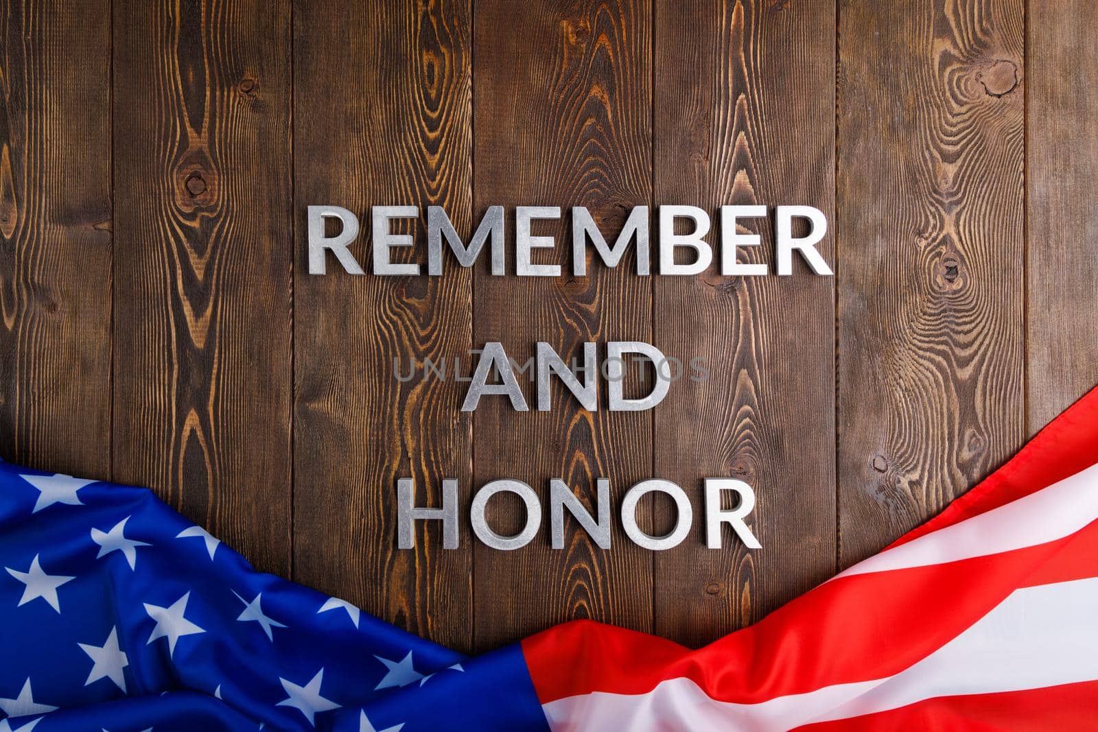 words remember and honor laid with silver metal letters on wooden background with USA flag underneath in high angle view