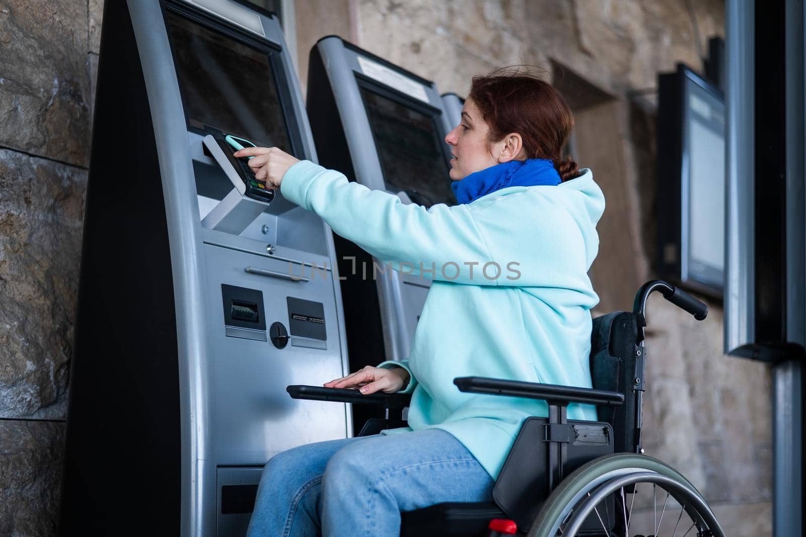 Caucasian woman in a wheelchair buys a train ticket using a mobile phone at a self-service checkout. by mrwed54