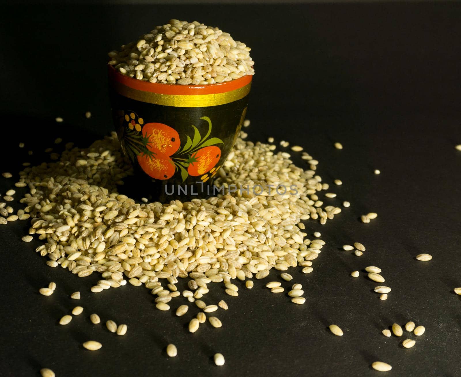 Scattered grains of oatmeal with a painted wooden cup on a black background.