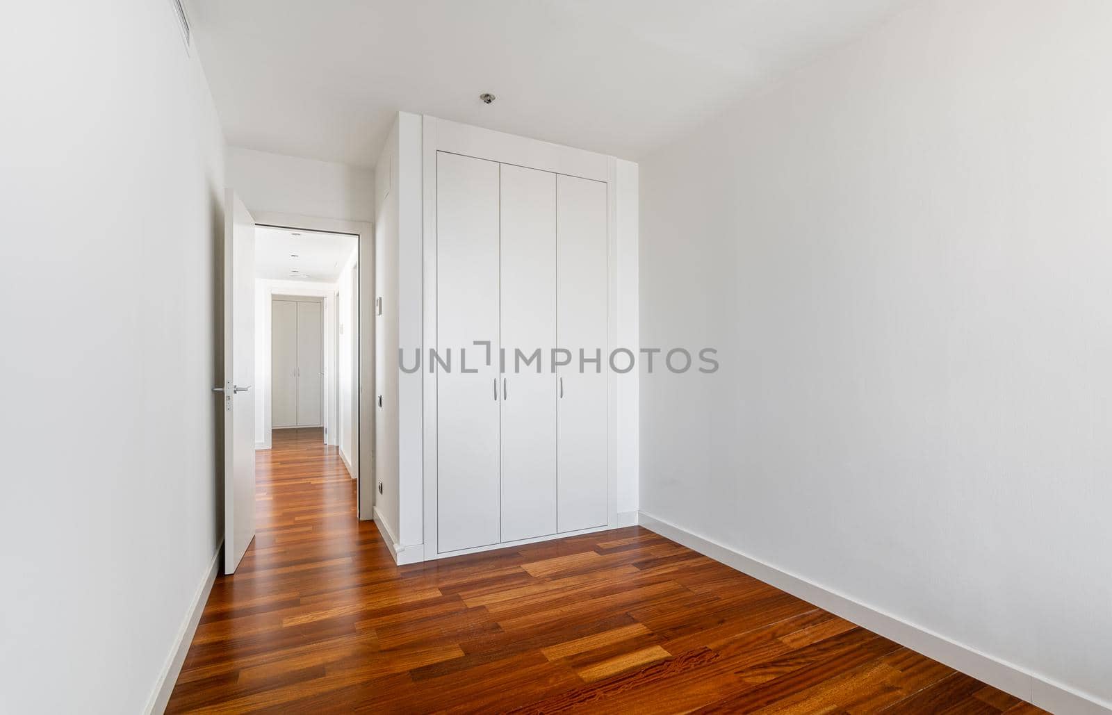 Interior of empty apartment, white room with built-in wardrobe, parquet floor and view to the hallway by apavlin