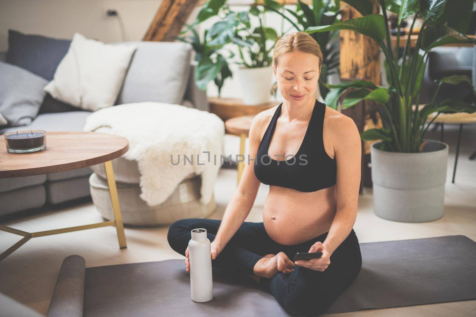 Young happy and cheerful beautiful pregnant woman chating to family and friends on mobile phone while staying fit, sporty and active on her maternity leave. Motherhood, pregnancy, yoga concept