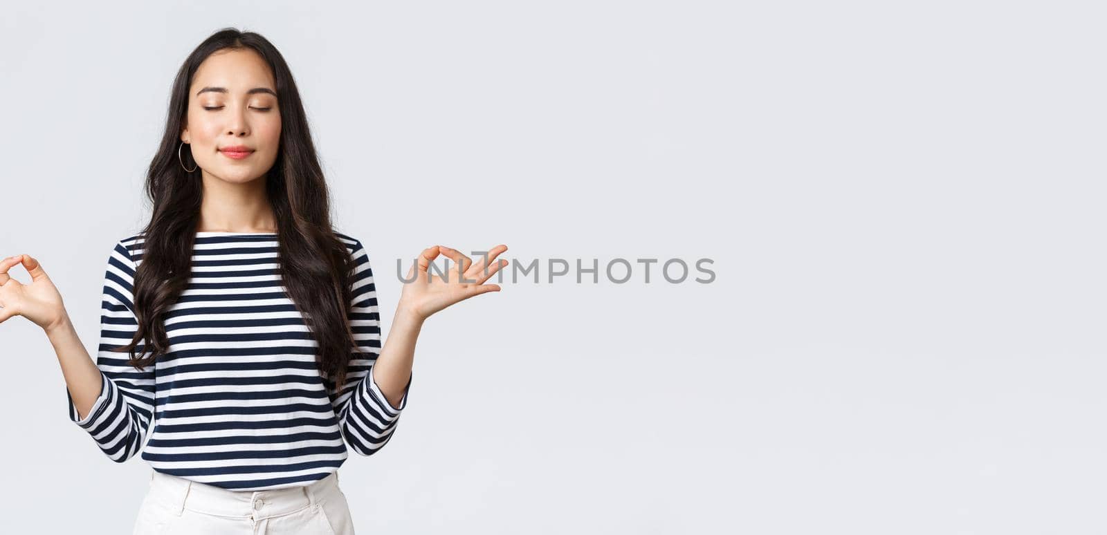 Lifestyle, people emotions and casual concept. Relaxed and patient smiling young asian woman with closed eyes meditating to calm down, do breathing exercises with hands in zen gesture.