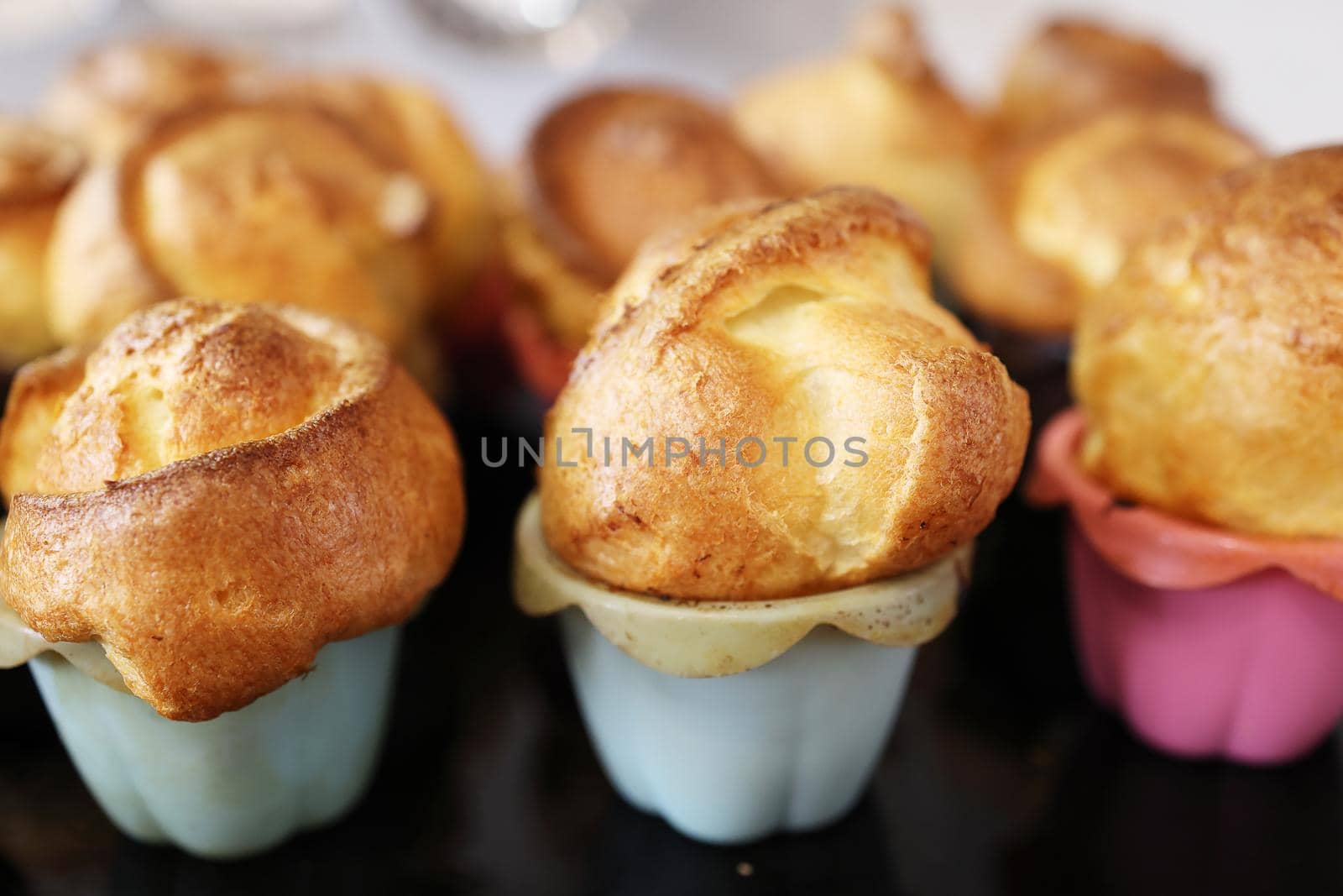 Homemade popover, which is a lush, airy and egg hollow roll, fresh from the oven. Yorkshire pudding freshly baked in silicone blue and pink baking dishes, selective focus