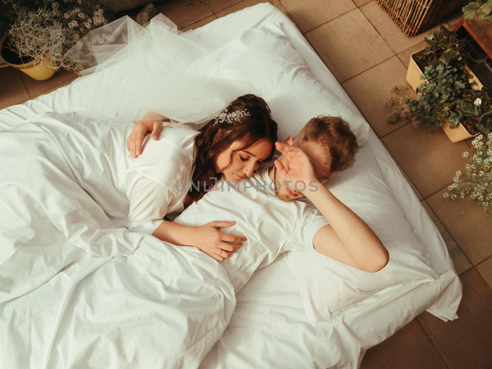 loving married couple lie on bed in hotel, relax together. man and woman in bathrobes have rest, leisure time, enjoy. grain effect by Symonenko