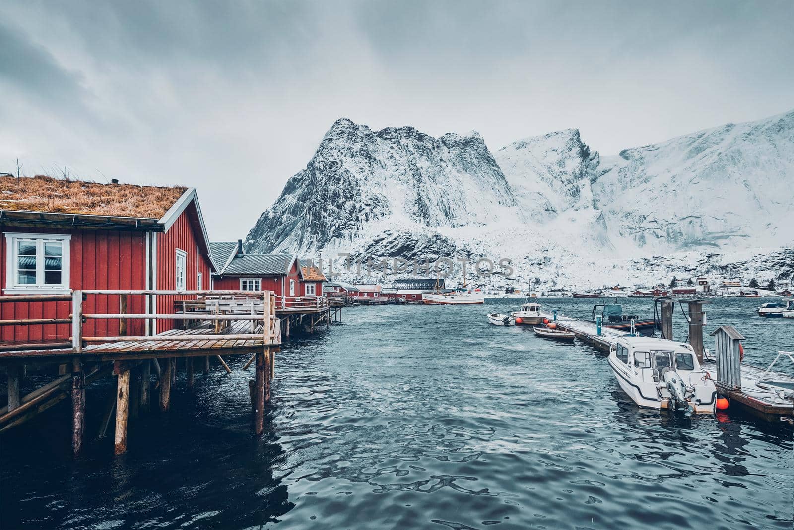 Traditional red rorbu houses in Reine fishing village in winter and pier with boats. Lofoten islands, Norway