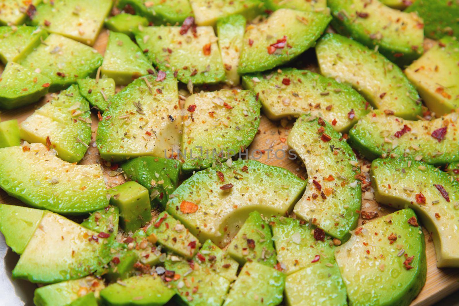 Close-up of sliced avocado pieces on a wooden cutting board. Avocado covered with spices and salt in shallow depth of field. Vegetarian background.