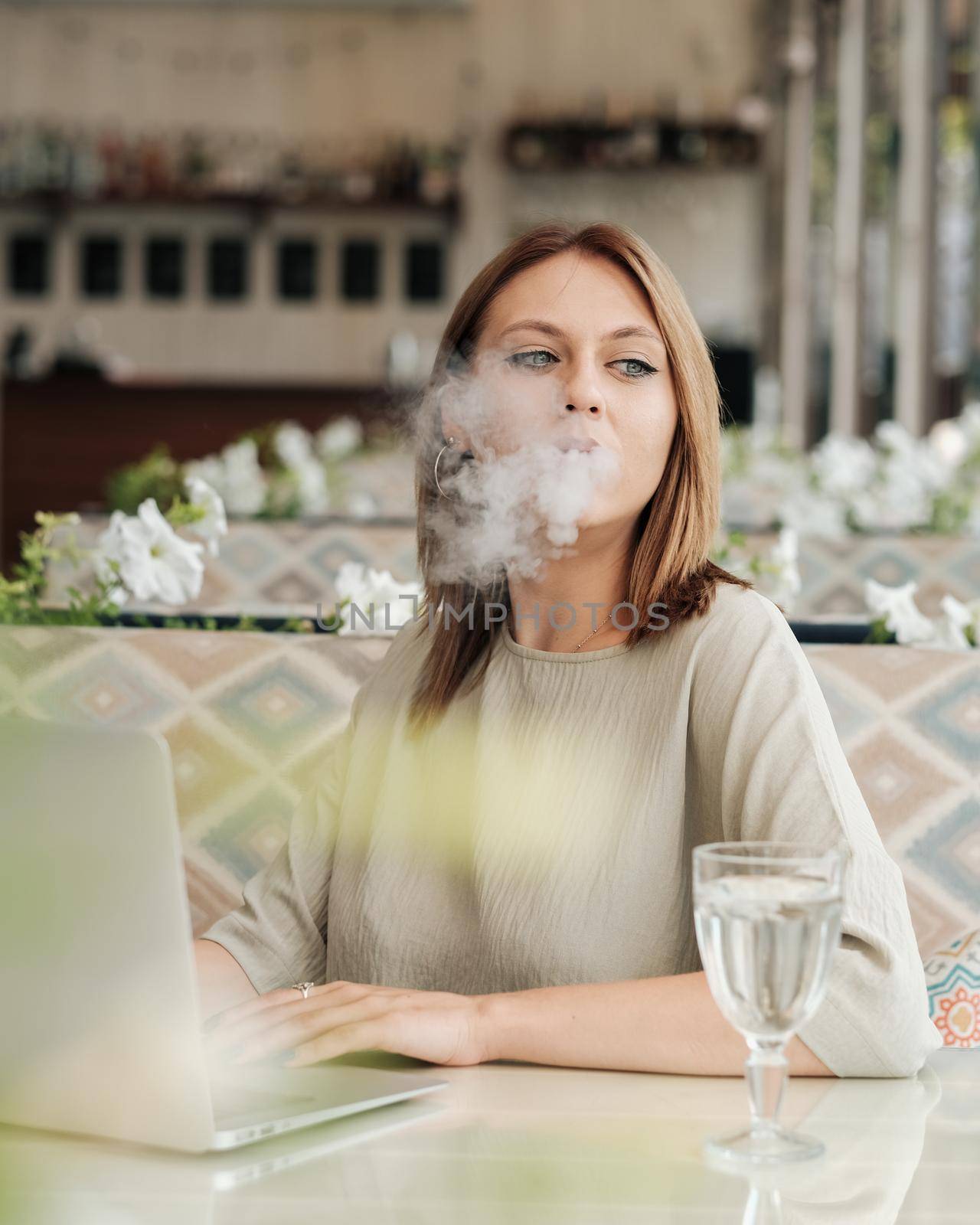 Young Woman Smoking Electronic Cigarette in the Restaurant While Working on Laptop by Romvy
