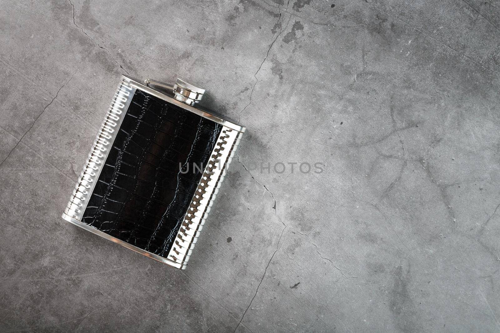 Steel flask in leather finish for alcohol on a dark background with copy space